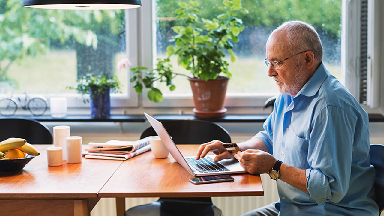 senior man paying bills with laptop and card