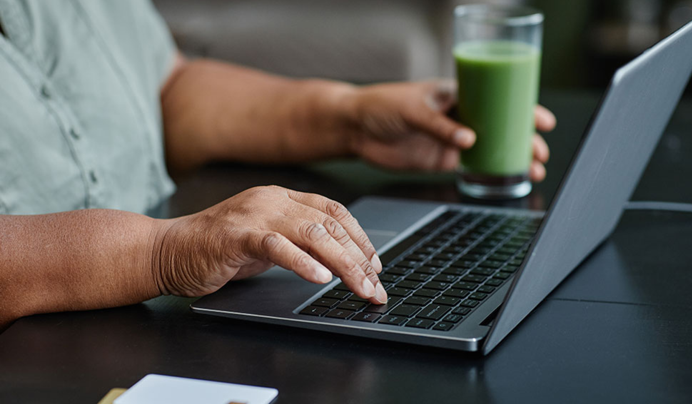 person using a laptop and holding a green juice