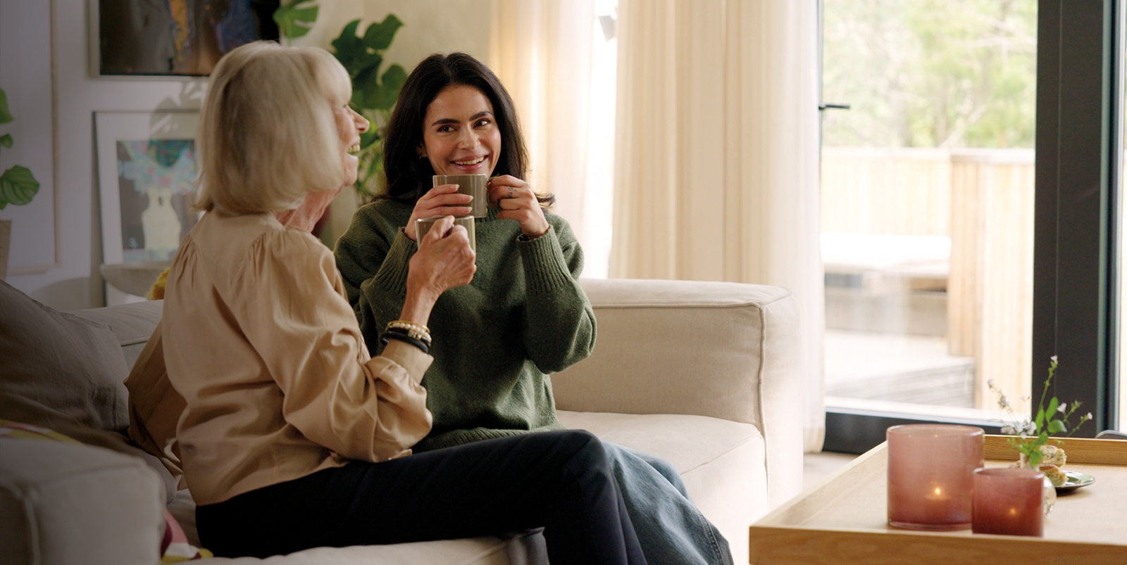 two women sitting on a couch drinking out of mugs