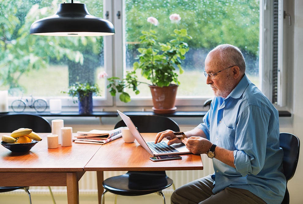 senior man paying bills with laptop and card