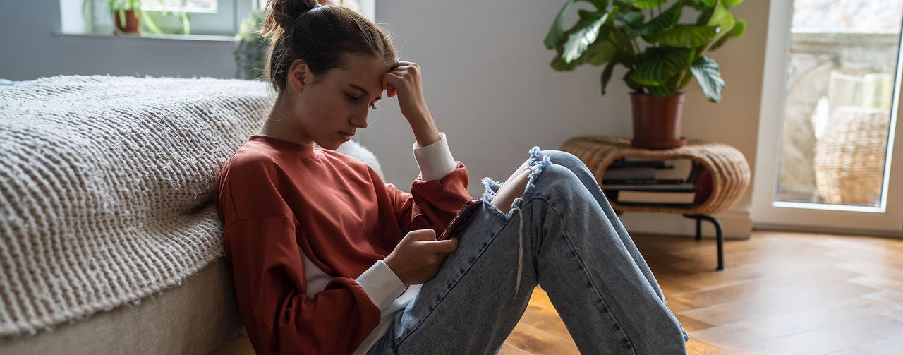 a young woman sitting on the floor looking at a smartphone.