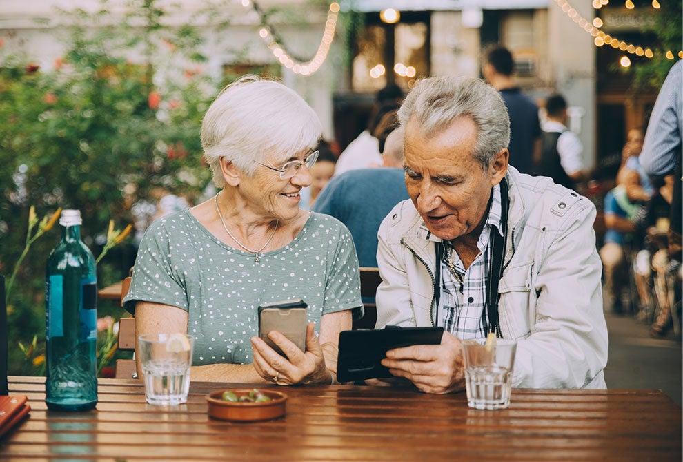 senior couple using devices at cafe