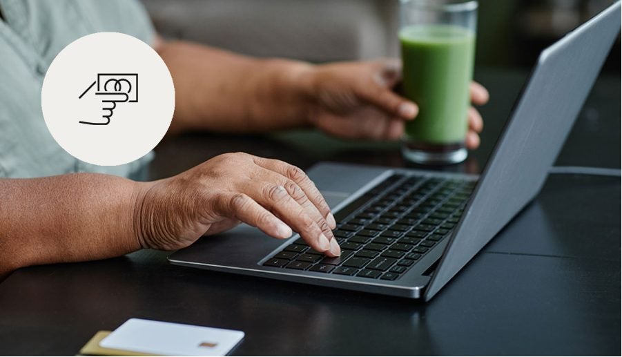 person using laptop while holding a glass of green juice