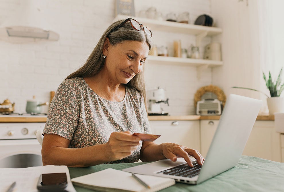 Woman typing on a laptop holding a card