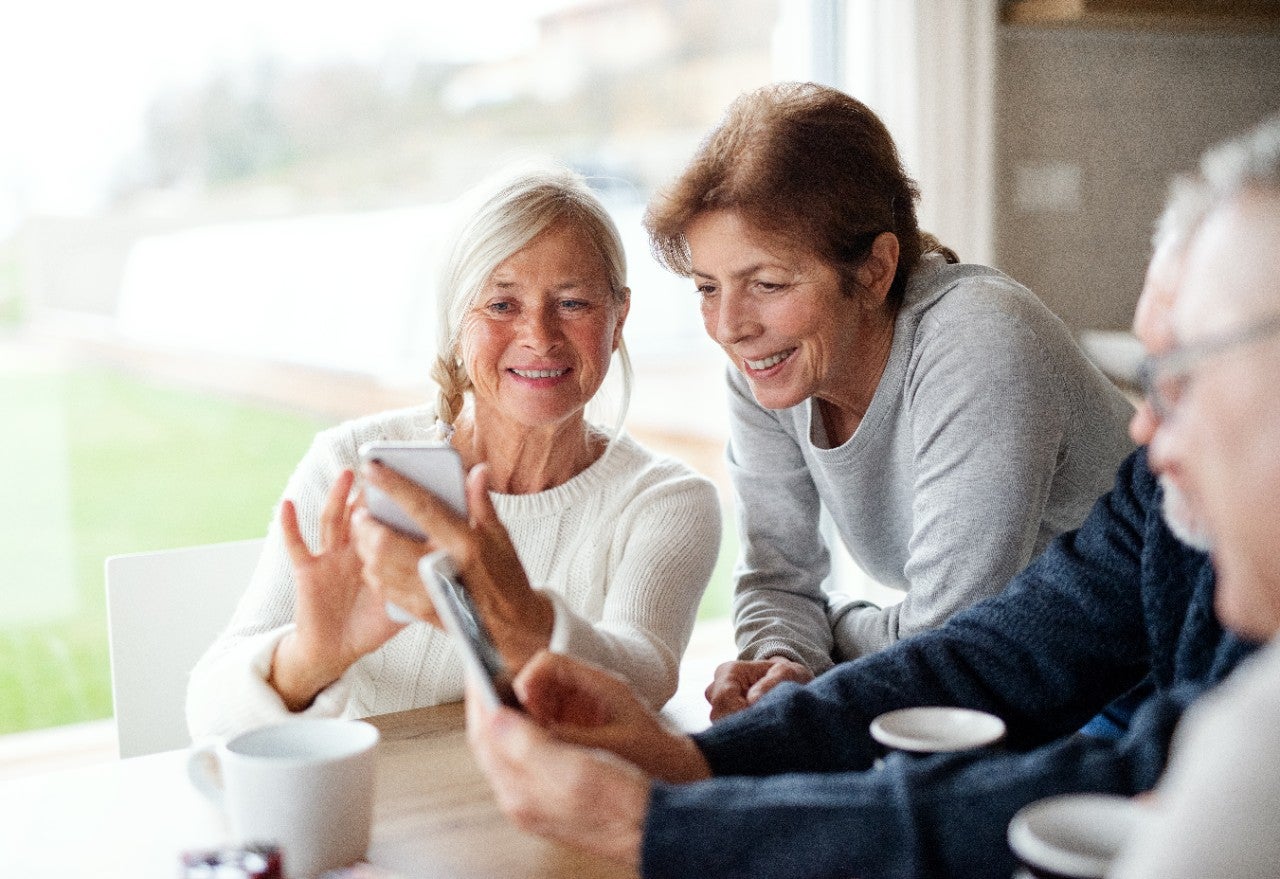 Group of senior friends at home, using smartphones.