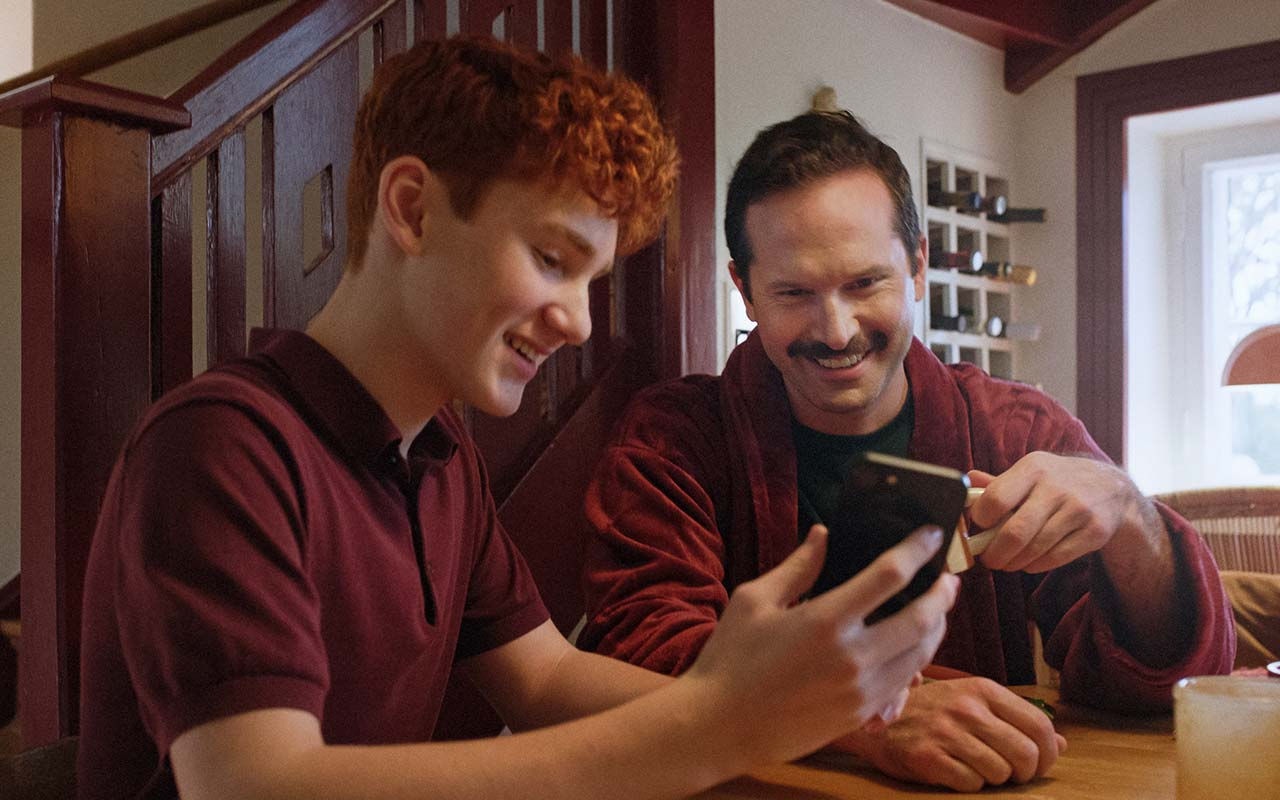 Två personer sitter vid ett bord med kaffe och tittar på en mobiltelefon.