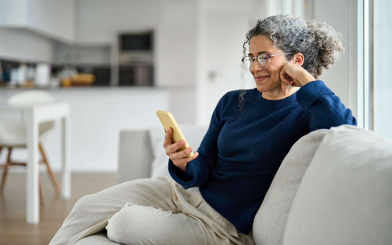 Person som sitter på en ljus soffa och tittar på en smartphone.