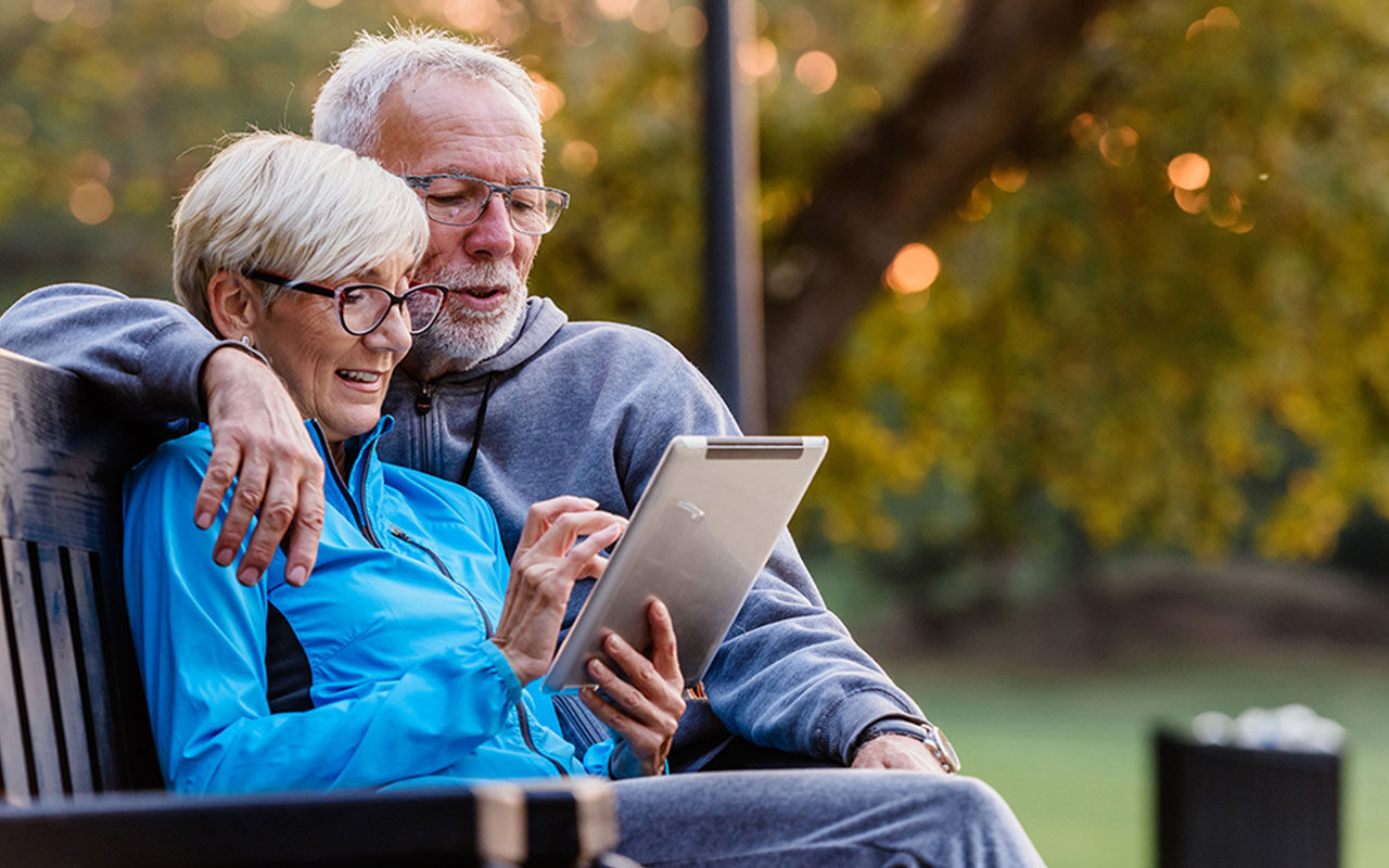Två personer sitter på en parkbänk och använder en surfplatta.