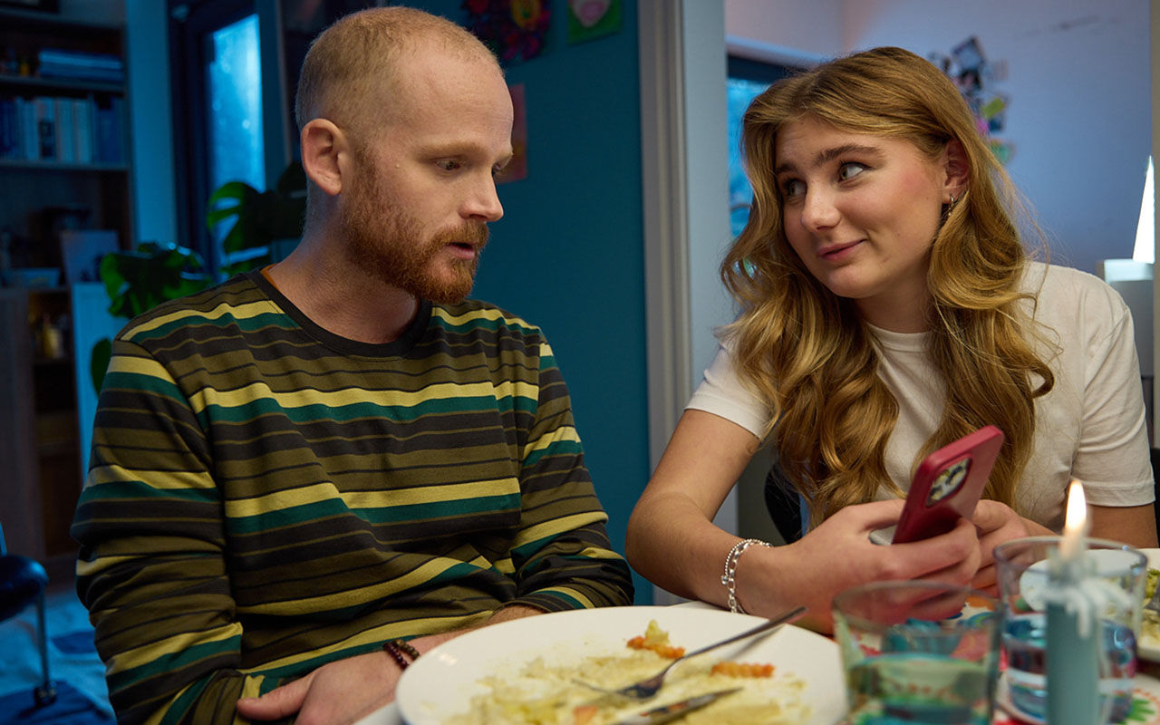 Två personer sitter vid ett matbord och tittar på en mobiltelefon.