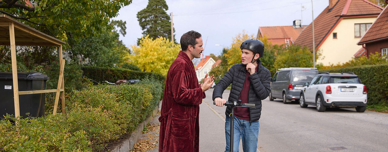 Två personer står på en gata, en håller i en elscooter.