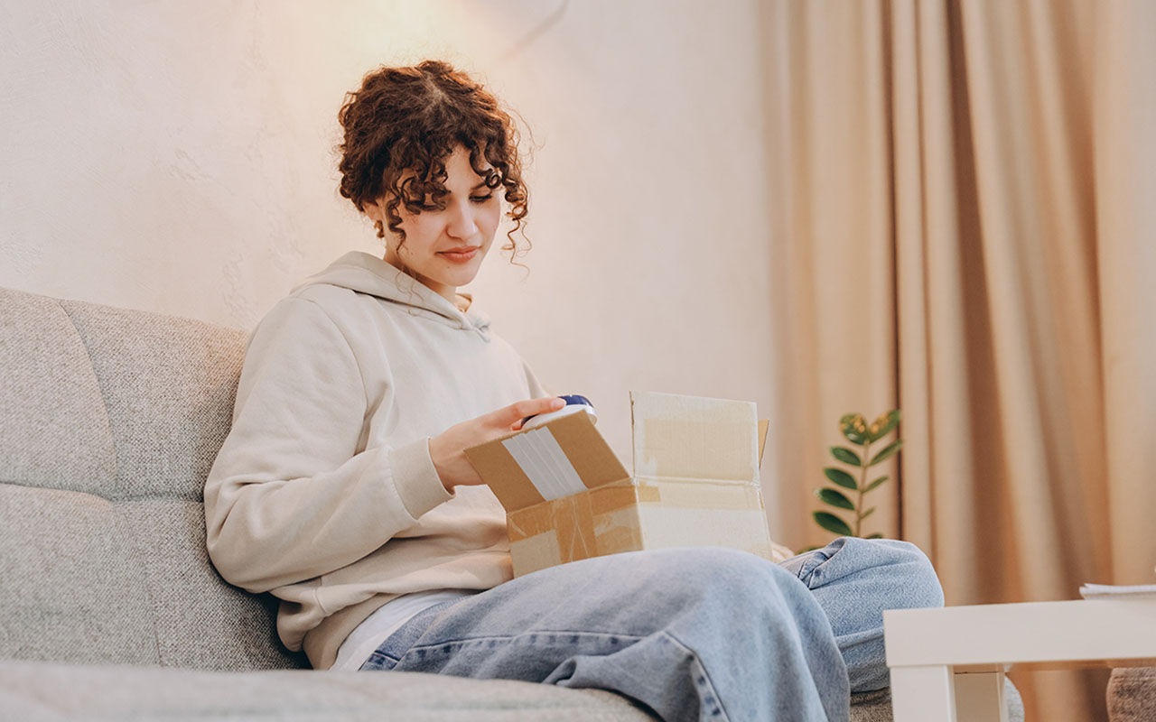 En person sitter i en soffa och öppnar en kartong.