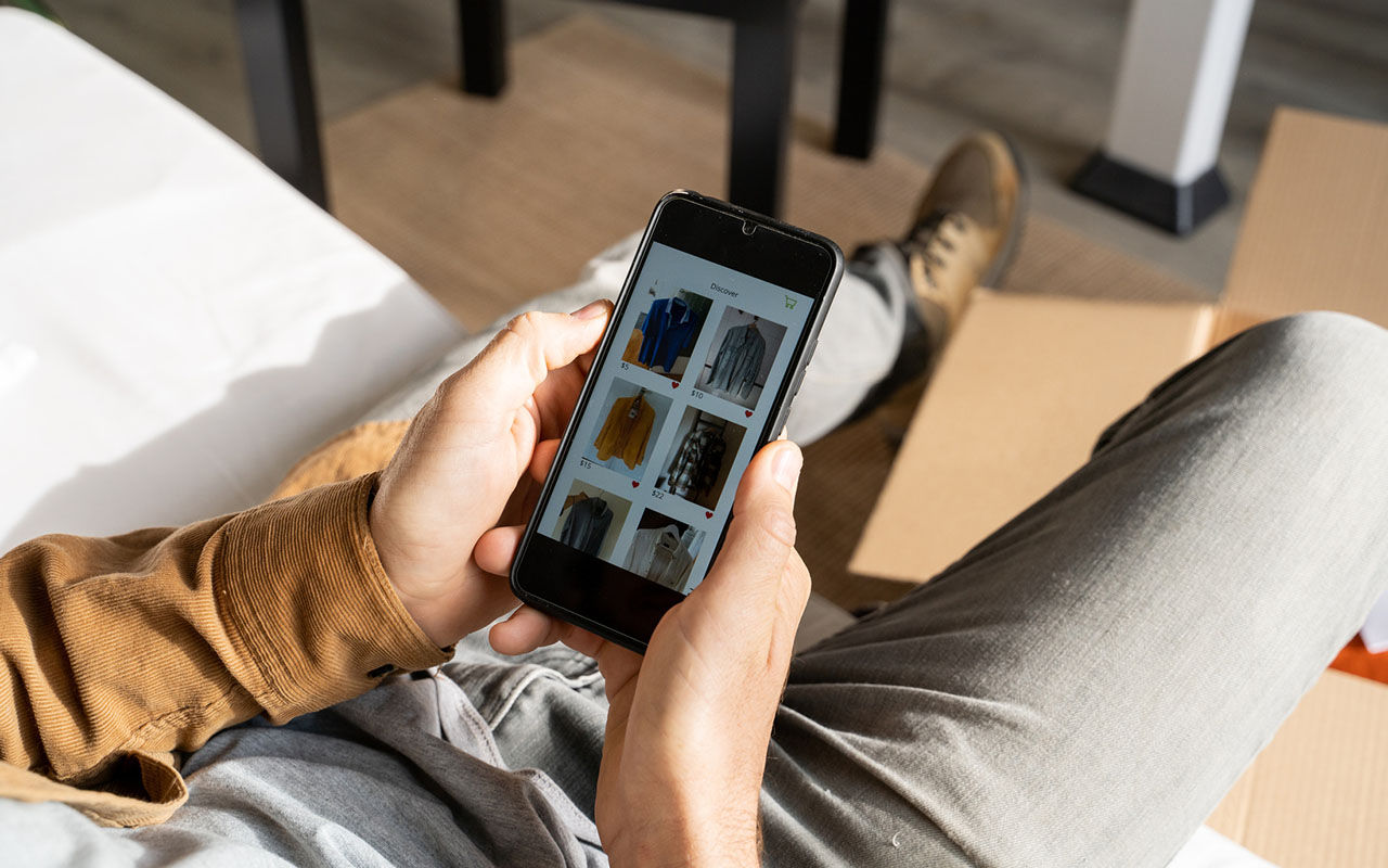 En person håller en smartphone och bläddrar bland kläder i en shoppingapp.
