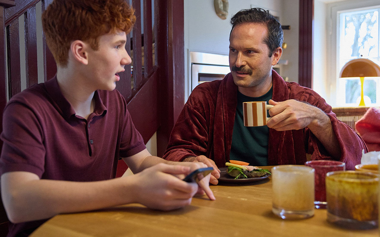 Två personer sitter vid ett bord med kaffe och tittar på en mobiltelefon.