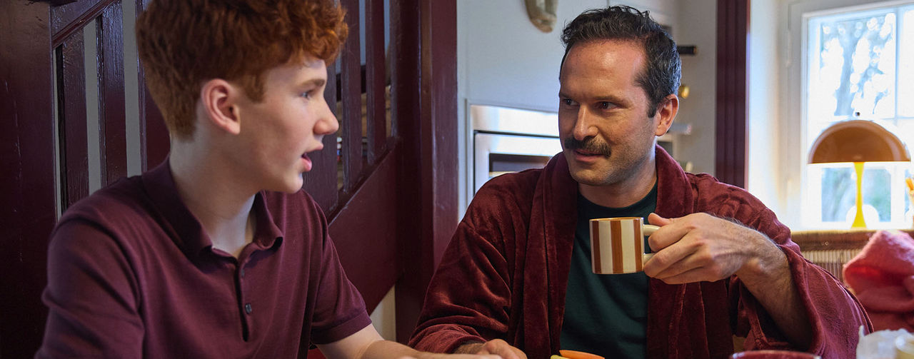 Två personer sitter vid ett bord med kaffe och tittar på en mobiltelefon.