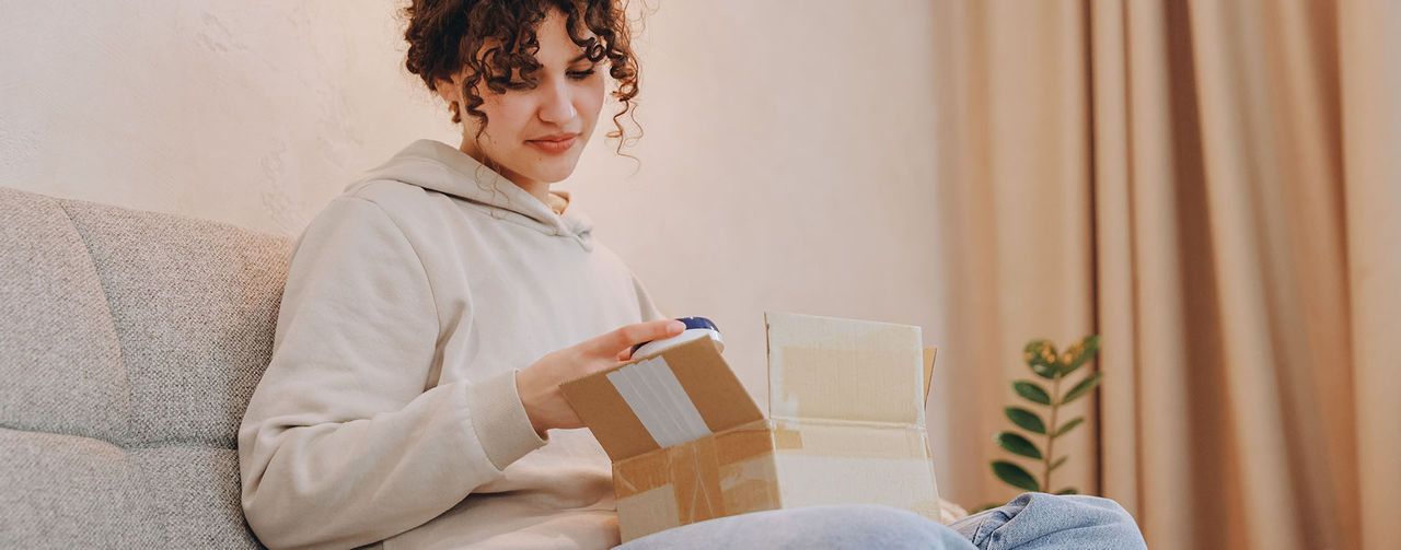 En person sitter i en soffa och öppnar en kartong.