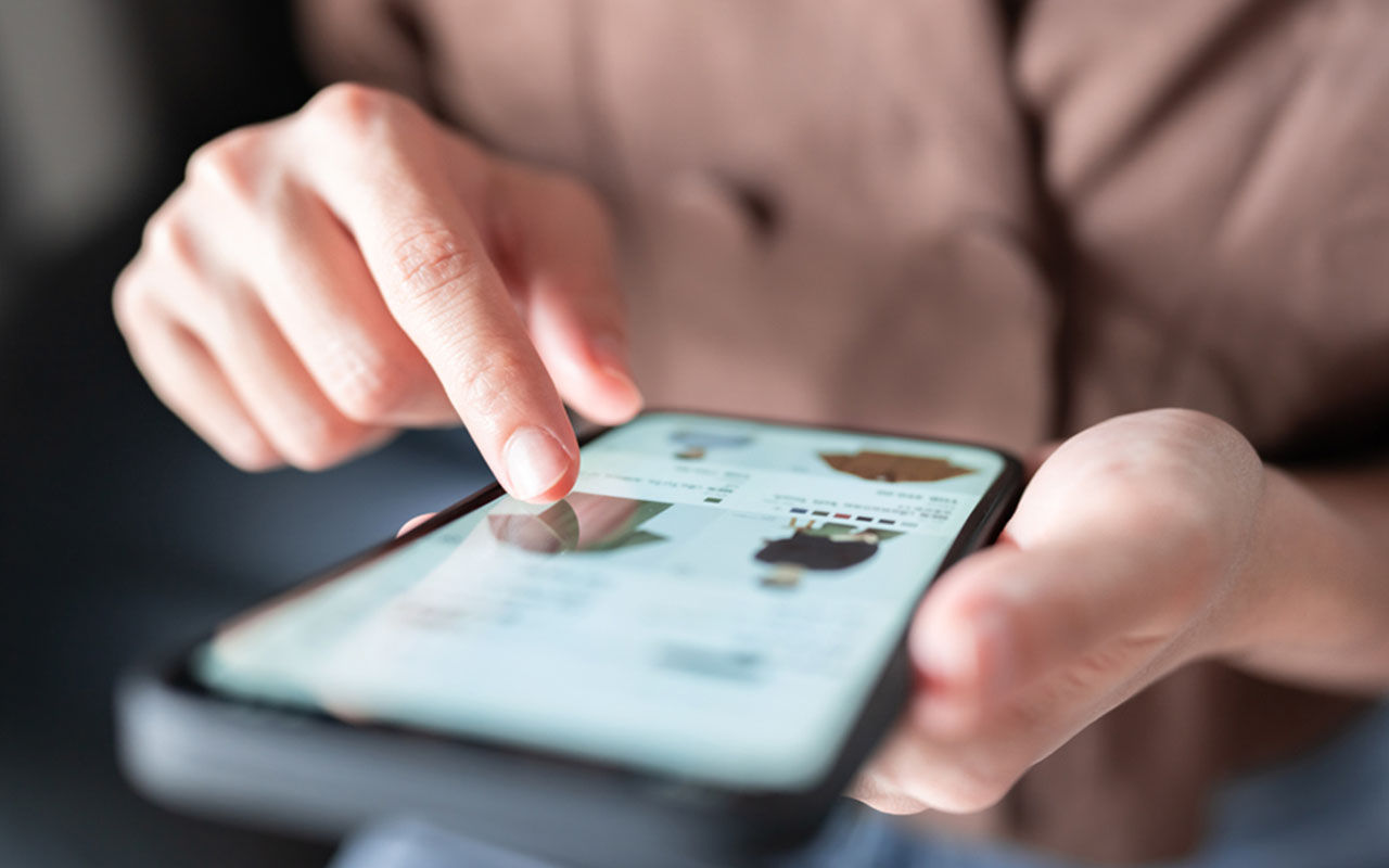 En hand pekar på en smartphone-skärm som visar en shoppingapp.