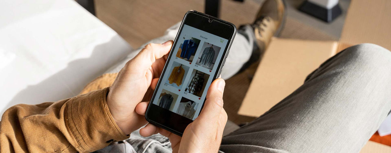 En person håller en smartphone och bläddrar bland kläder i en shoppingapp.